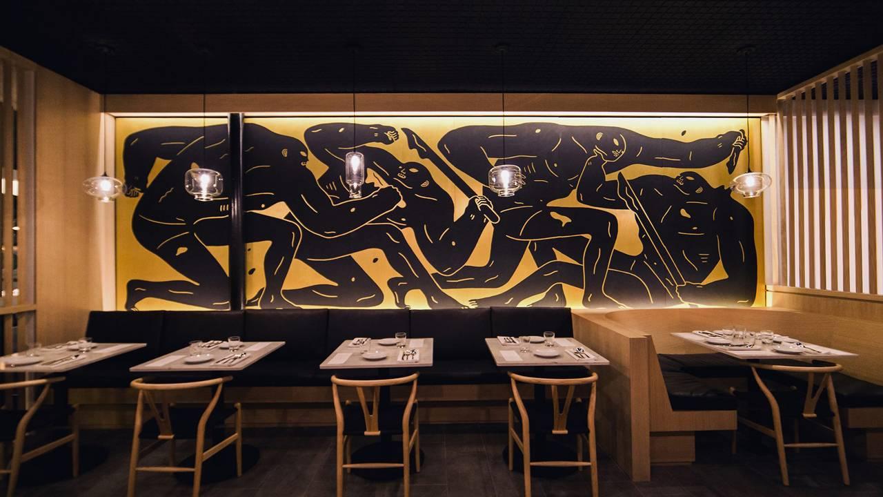 A restaurant with a bold mural wall, pendant lighting, and wooden chairs around set tables at Bone Kettle.