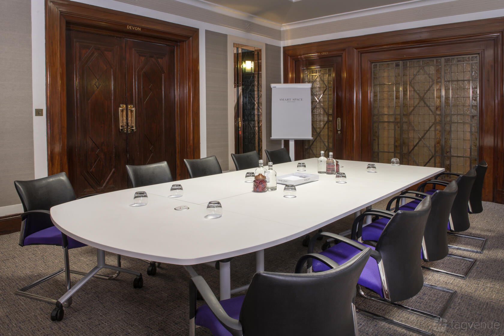 A conference room with a long white meeting table, black chairs, and wood-paneled doors at Grand Connaught Rooms.