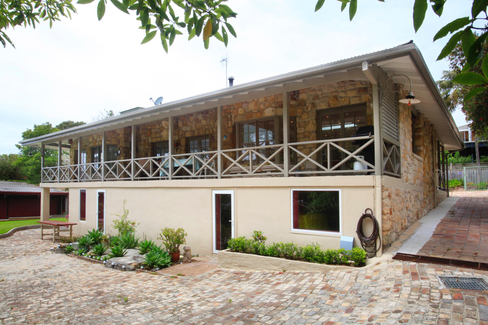 A recording studio with a stone exterior, wraparound porch, and cobblestone courtyard at Jaminajar Music Production.