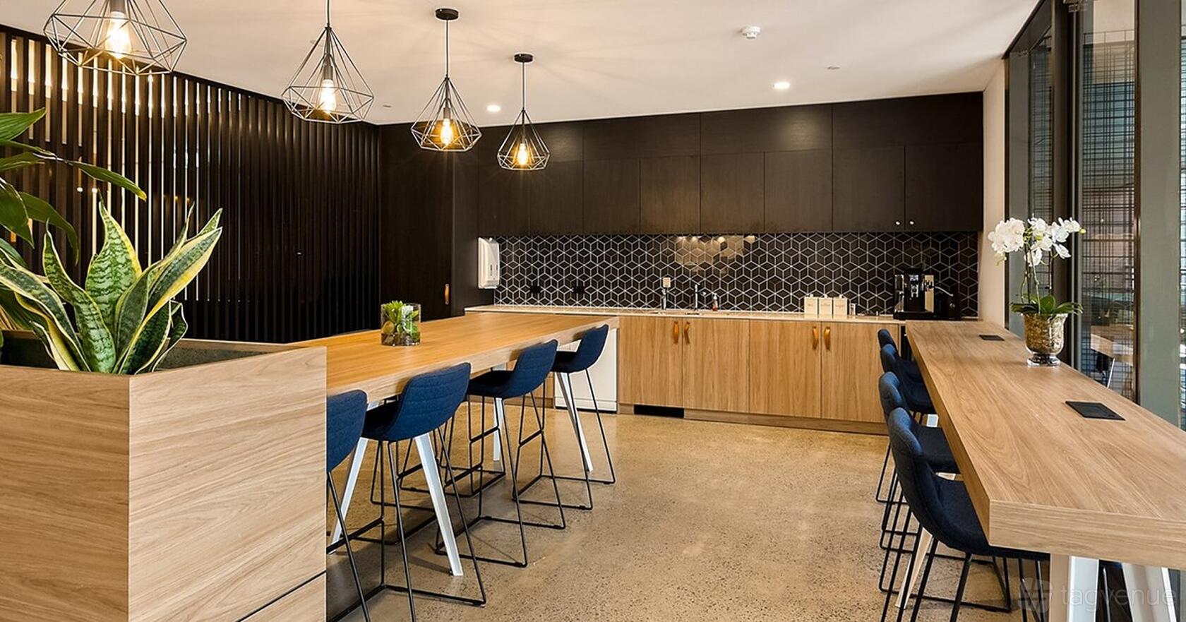An event space with high wooden tables, blue bar stools, pendant lighting, and a geometric tile backsplash at Workspace365 66 Clarence St.