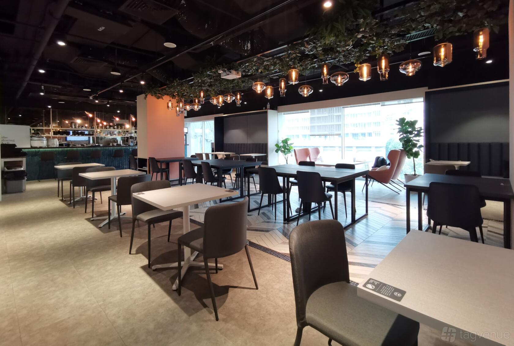 An event space with hanging pendant lights, greenery overhead, and large windows with city views at Workcentral.