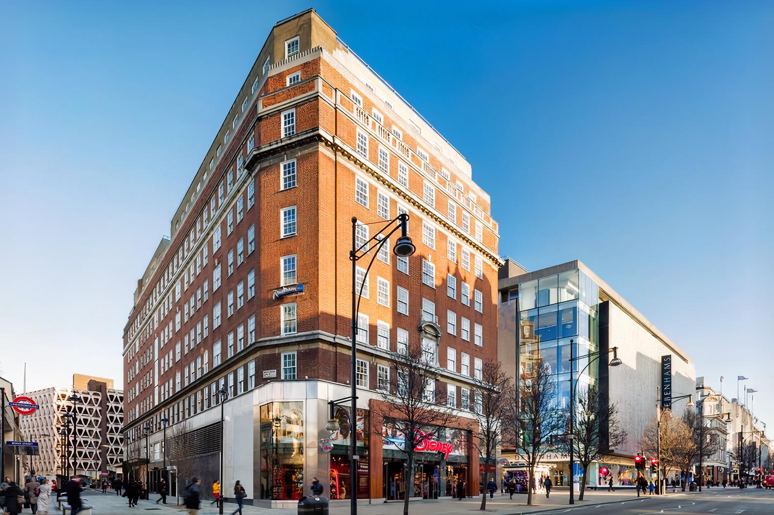 A red-brick hotel with large windows and ground-floor retail on a busy street at Radisson Blu Hotel, London Bond Street.