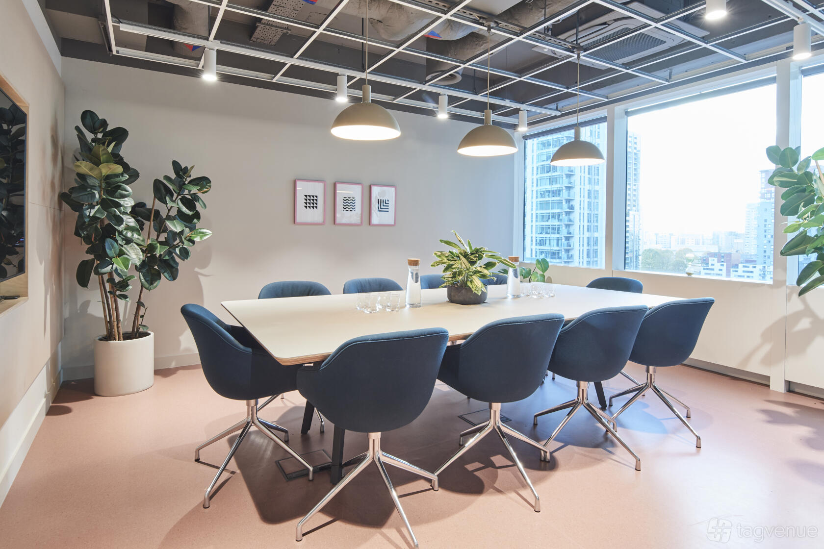 A coworking space meeting room with navy chairs, a large table, pendant lights, and city views at TYPE at Sierra Quebec Bravo.