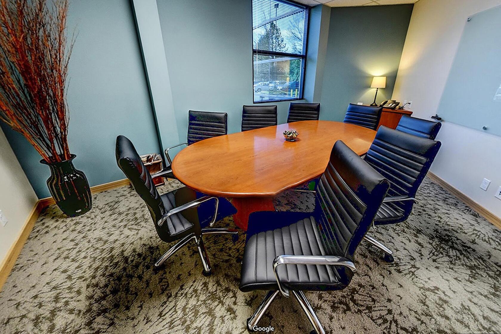 A meeting room with a wooden oval table, black leather chairs, and a window at Premier Workspaces - Northcreek.