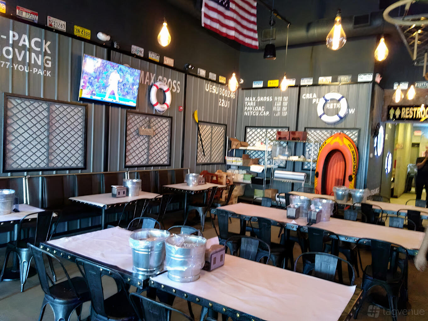 A restaurant with nautical decor, hanging lights, life rings, and long tables with metal chairs at Hook & Reel- Revere.