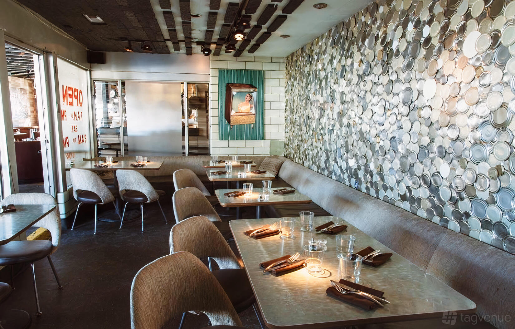 A dining room with a long banquette, tables set with glassware, and a decorative metal wall at Root Down.