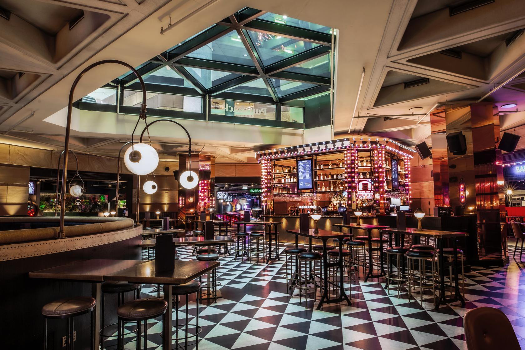 An event venue with checkered floors, modern pendant lighting, and a central illuminated bar at Puttshack Bank.