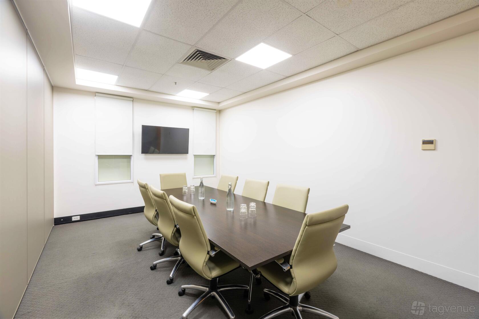 A boardroom with a dark conference table, beige leather chairs, and wall-mounted TV at Business Centre @ 365.