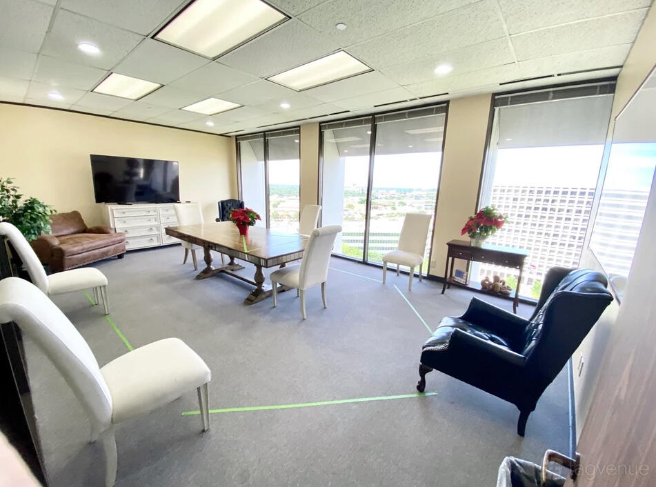 A meeting room with floor-to-ceiling windows, a long wooden table, white chairs, and city views at Office In America Co.