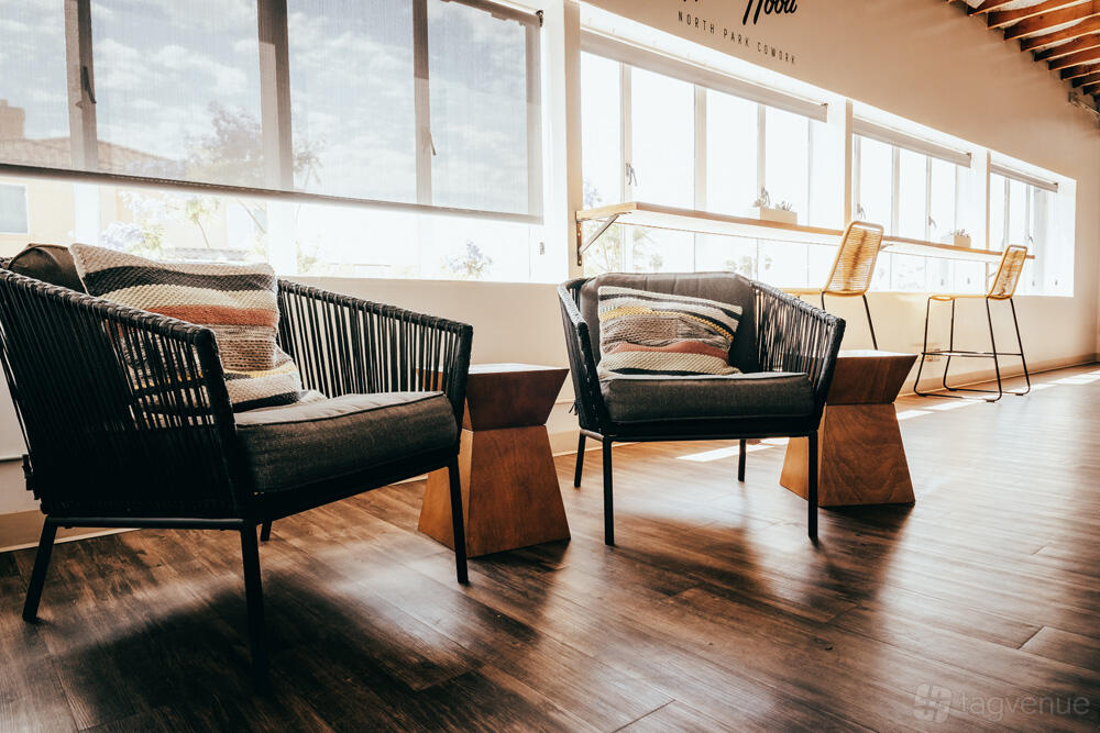 A function room with wicker lounge chairs, wooden side tables, large windows, and natural light at Hardihood Cowork - North Park, San Diego.