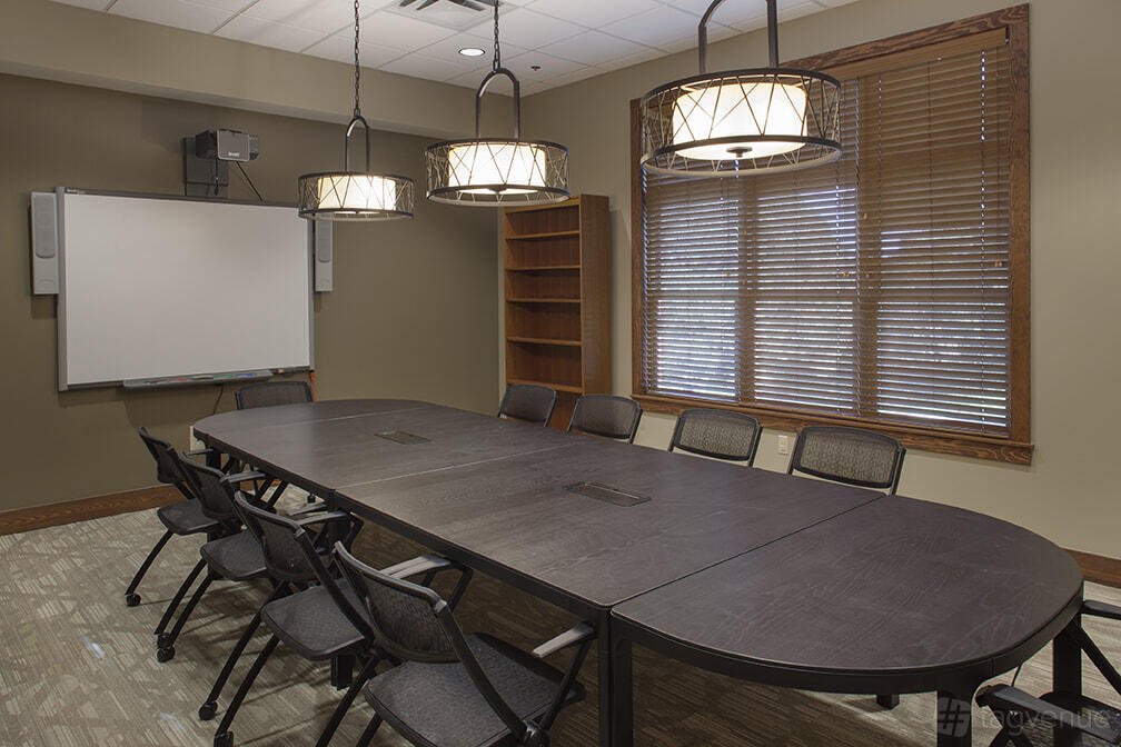 A conference room with a long oval table, black chairs, and large windows with wooden blinds at Zilker Lodge.