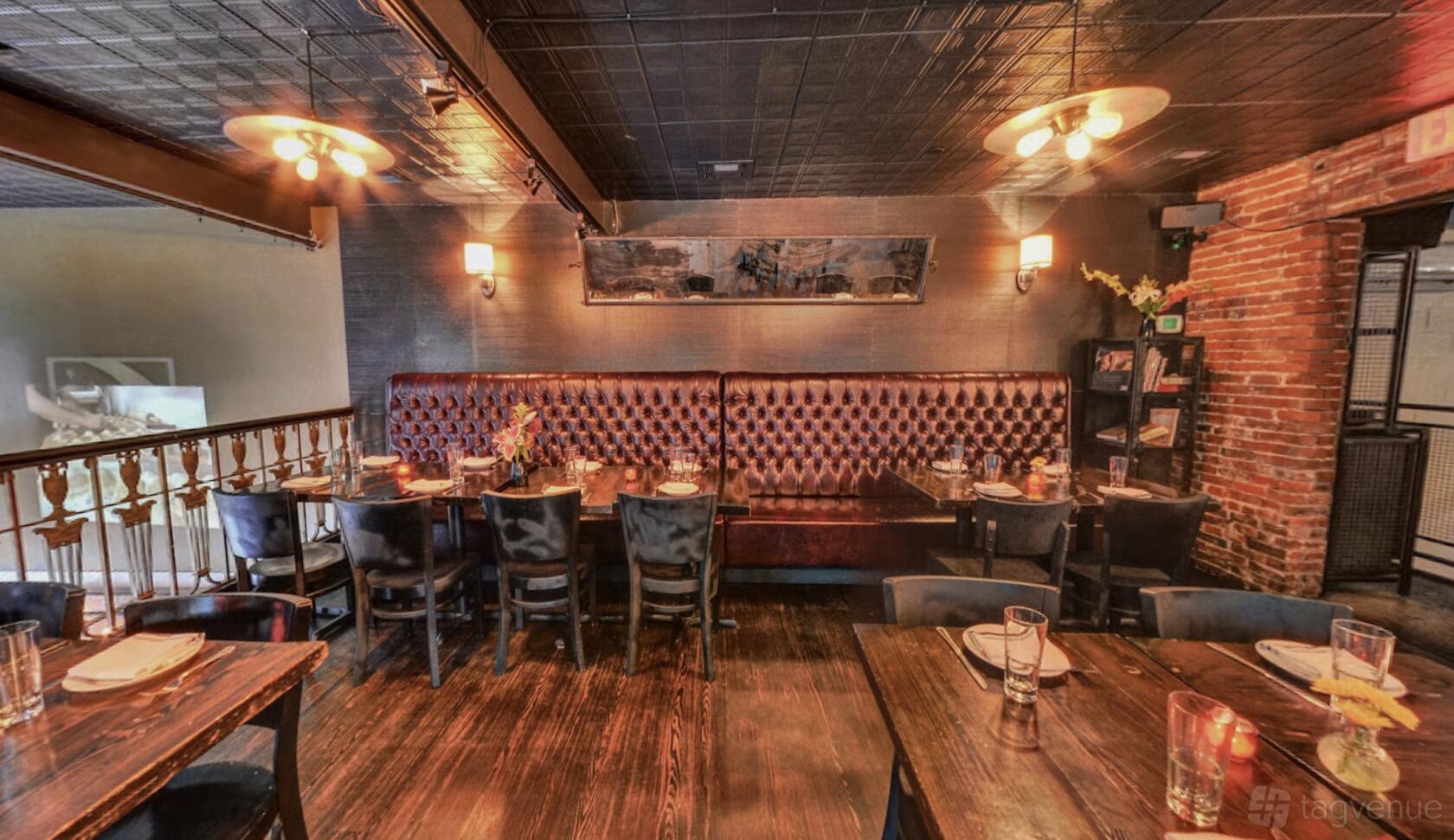 A dining room with tufted leather banquette seating, exposed brick, and dark wood tables at Jerry's Bar.