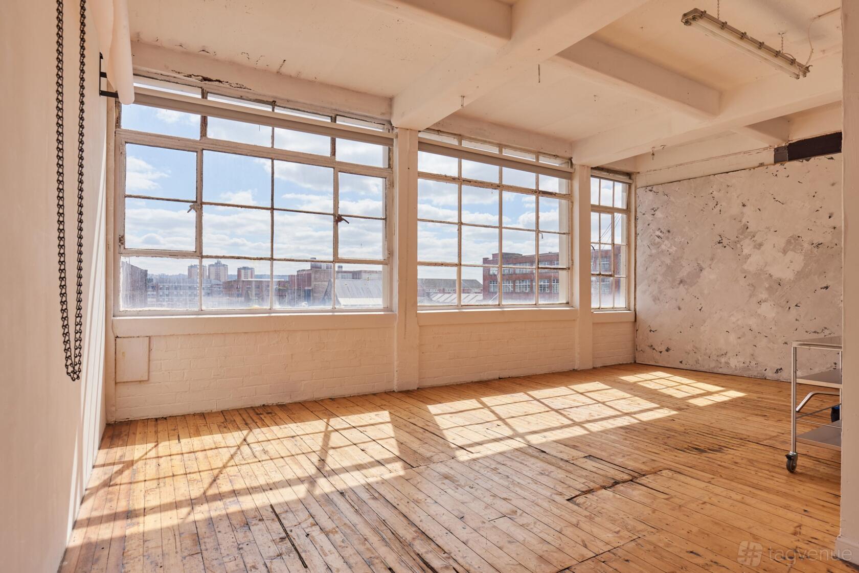 A photo studio with large industrial windows, white walls, and hardwood floors at Broadscope Studios.