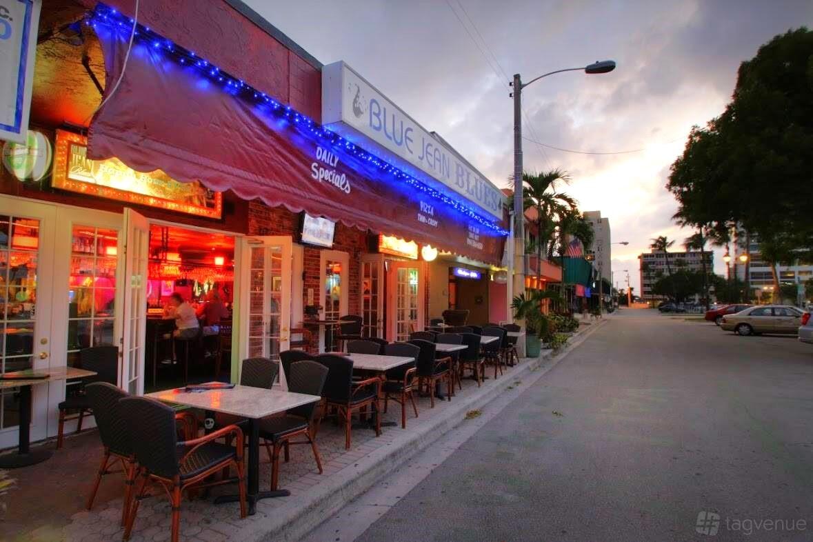 An outdoor seating area with wicker chairs and square tables along the sidewalk at Blue Jean Blues.