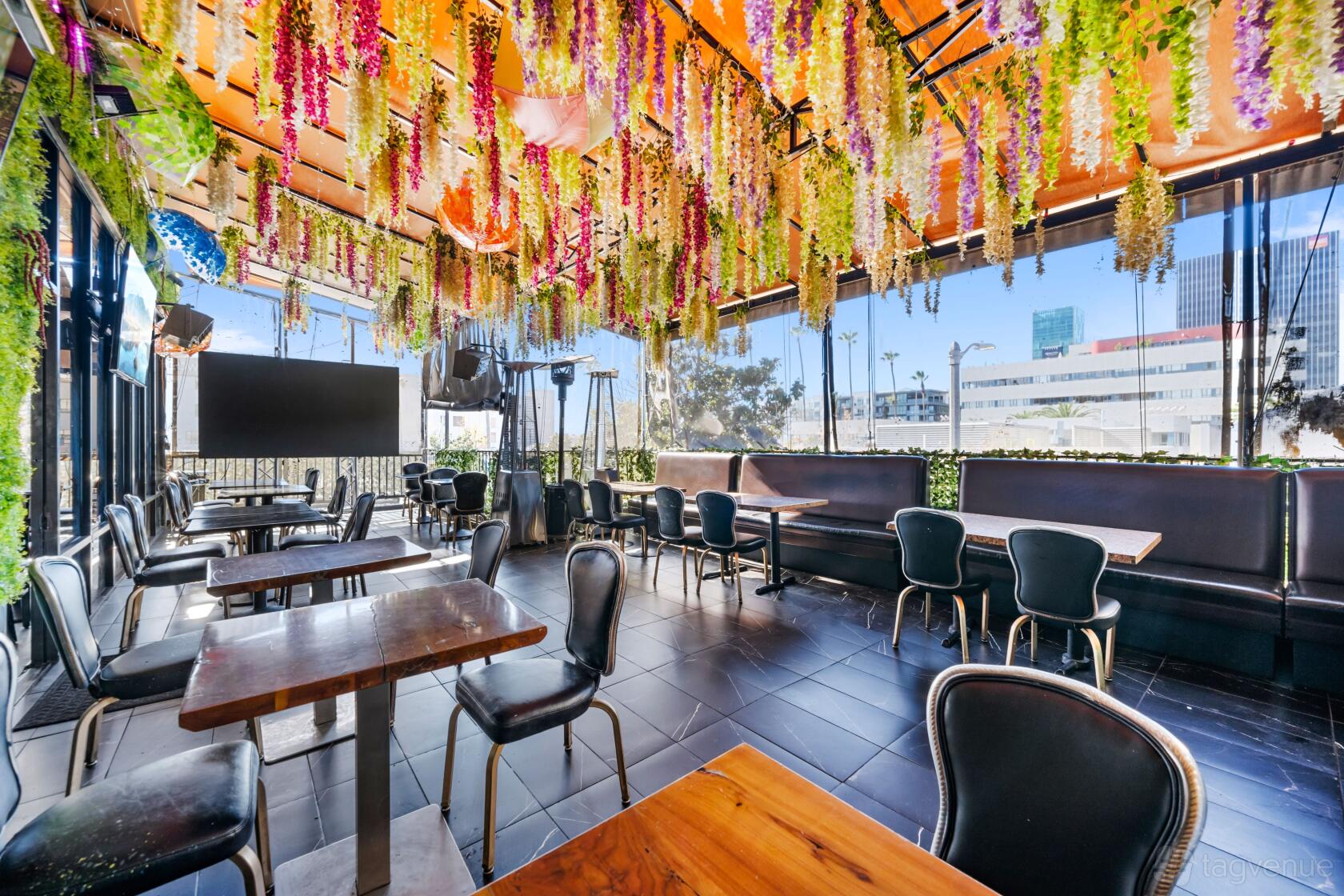 A terrace with hanging floral decor, wooden tables, and city views at Sunset Rooftop.