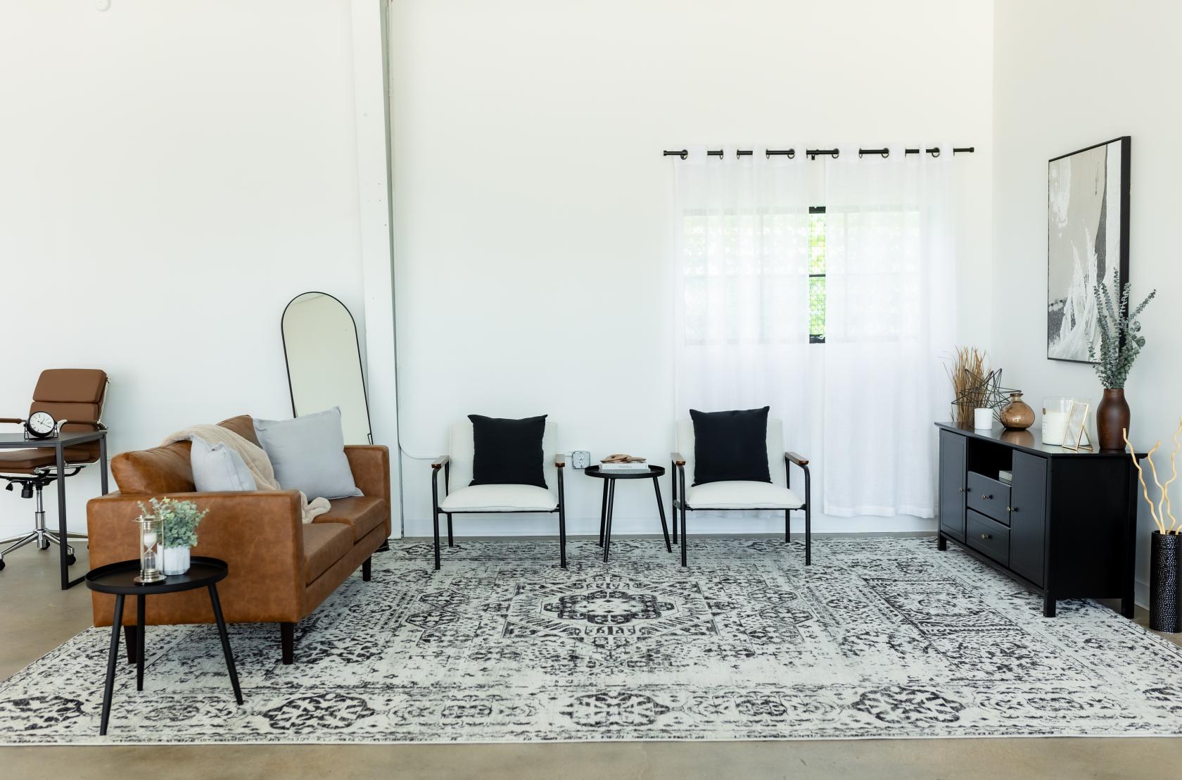 A photo studio with a tan leather sofa, patterned rug, and sheer curtains at Brightside Studios Dallas.