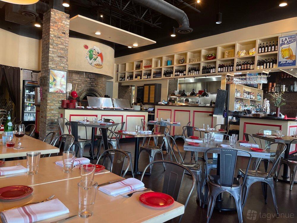 A restaurant dining area with metal chairs, set tables, open kitchen, and a wood-fired pizza oven at Numero 28 Allen Ristorante Pizzeria.