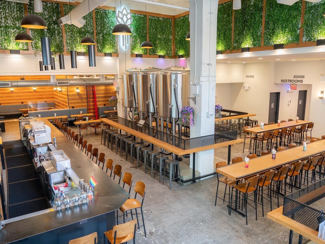 A bar in a brewery with stainless steel brewing tanks, hanging greenery, and communal wooden tables at Torch and Crown.