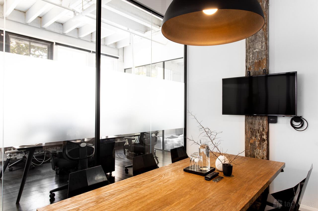 A meeting room with a wooden table, glass walls, and a mounted TV at Desk Space.