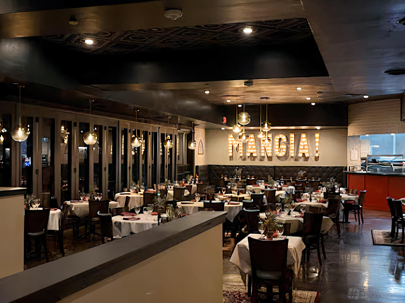 A restaurant dining room with round tables draped in white linens, pendant lighting, and a 'MANGIA!' sign at Pomodoro's Cucina Italiana.