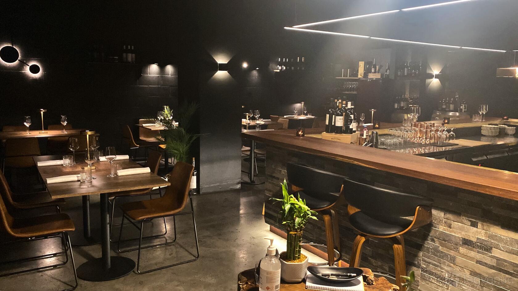 A restaurant with wood tables, leather chairs, and a long bar with backlit shelves at D.Vino Bistro & Vinoteca.