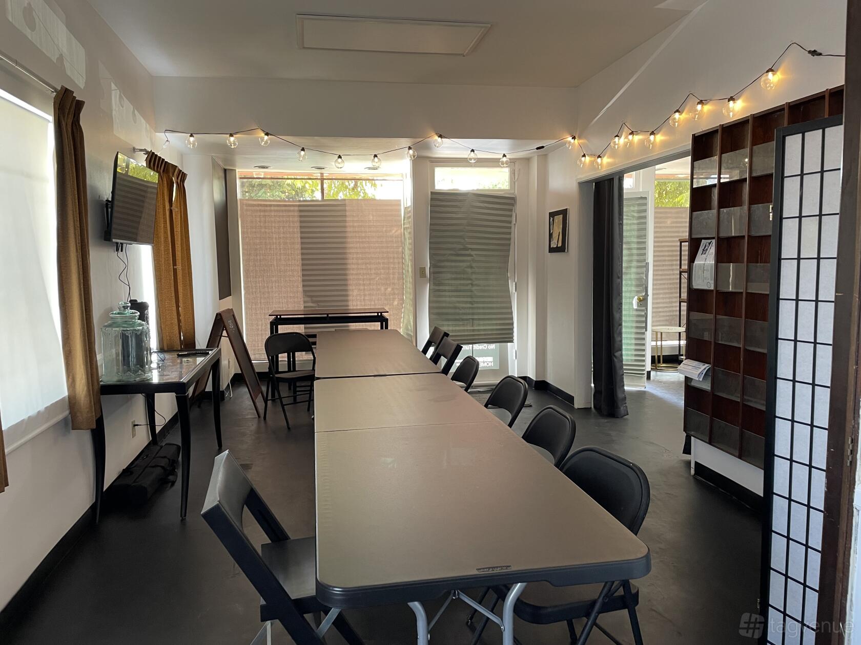 A meeting room with folding tables, black chairs, string lights, and natural light at Starms Business Center.