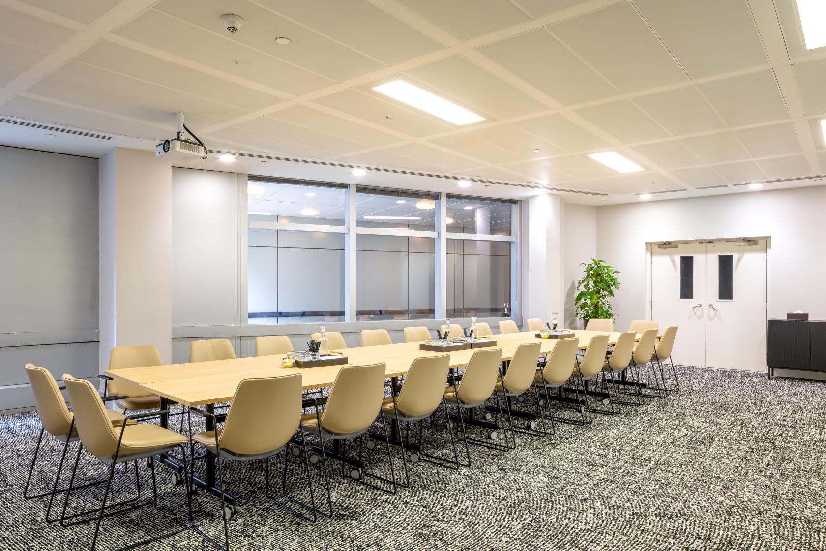 A meeting room with a long conference table, beige chairs, large windows, and ceiling lights at Landmark: 99 Bishopsgate, London.