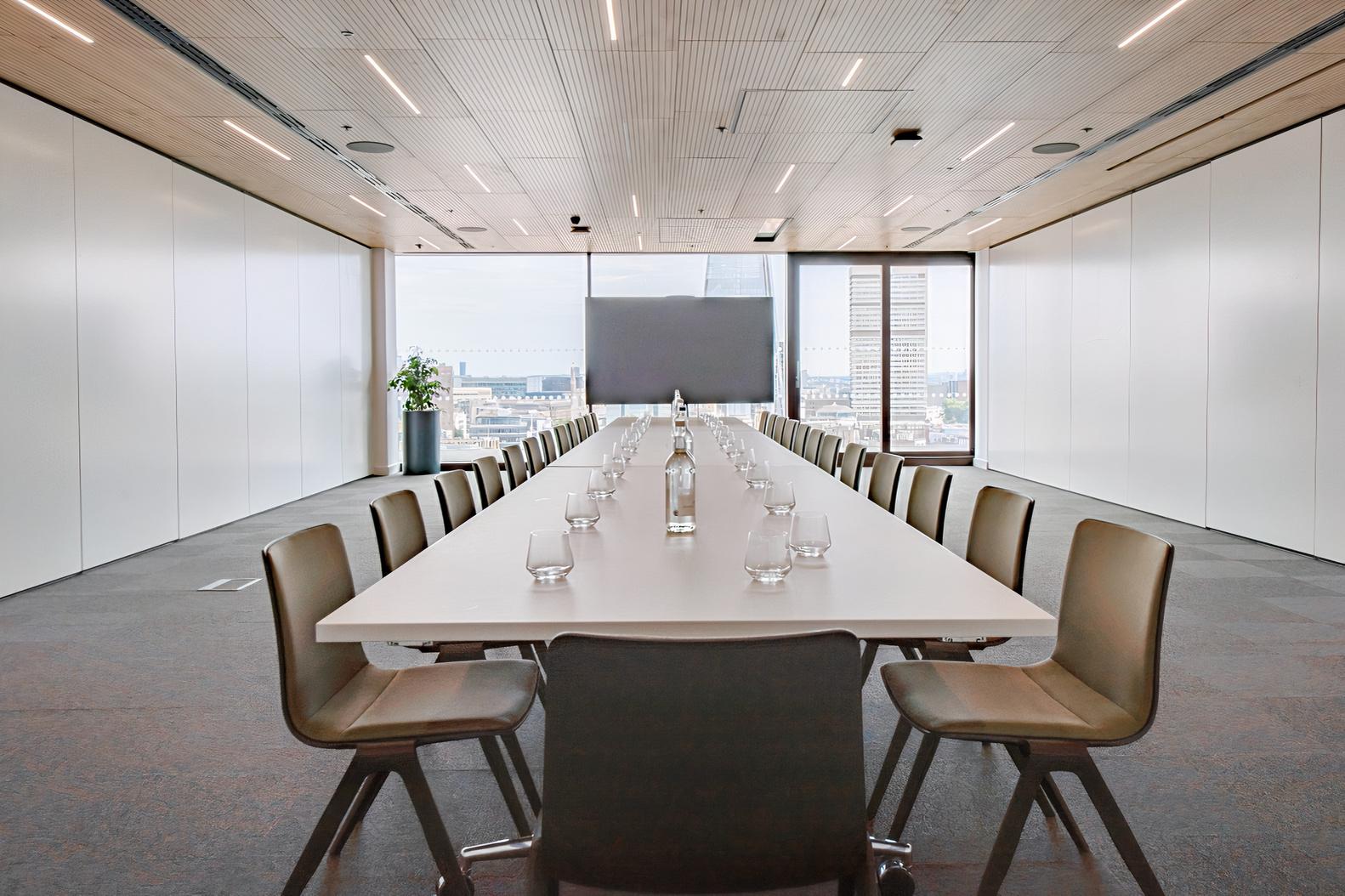 A meeting room with a long rectangular table, brown chairs, and floor-to-ceiling windows at Rose Court Events.