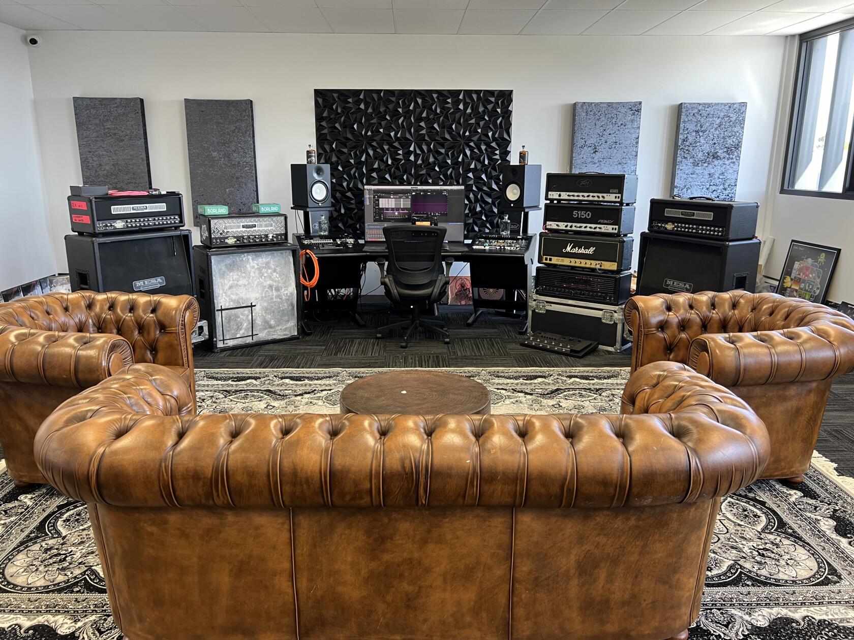 A rehearsal studio with brown leather sofas, soundproof wall panels, and music equipment at Unreil Studios.