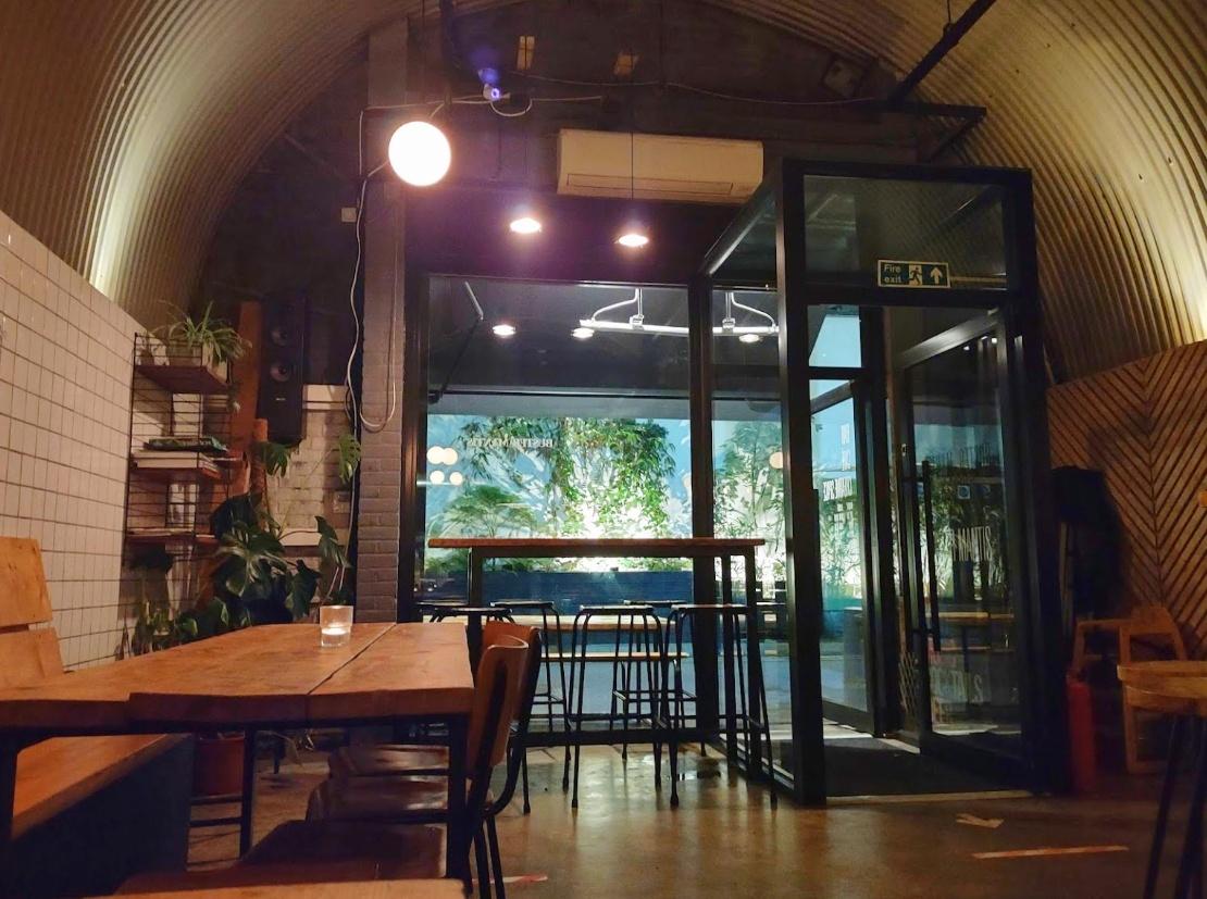 A restaurant with wood tables, tiled walls, and large windows looking out to a patio at Buster Mantis.