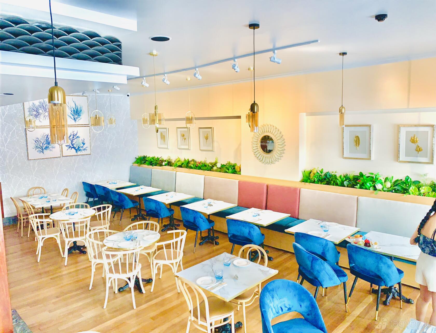 A restaurant dining area with wooden floors, velvet chairs, pastel banquettes, and framed artwork at Missony Restaurant.