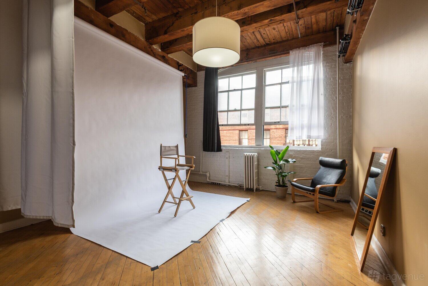 A photo studio with a seamless white backdrop, director’s chair, wooden floors, and large windows at Lumber Studios.