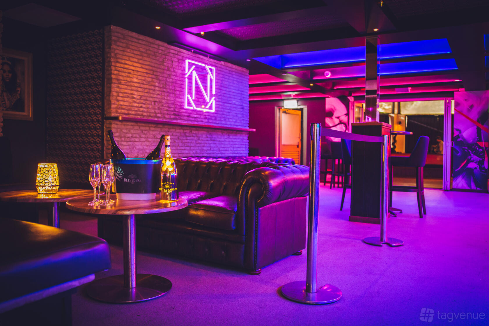A lounge in a bar with plush leather sofas, a neon wall sign, and a low table set with glasses at Niche Bar.