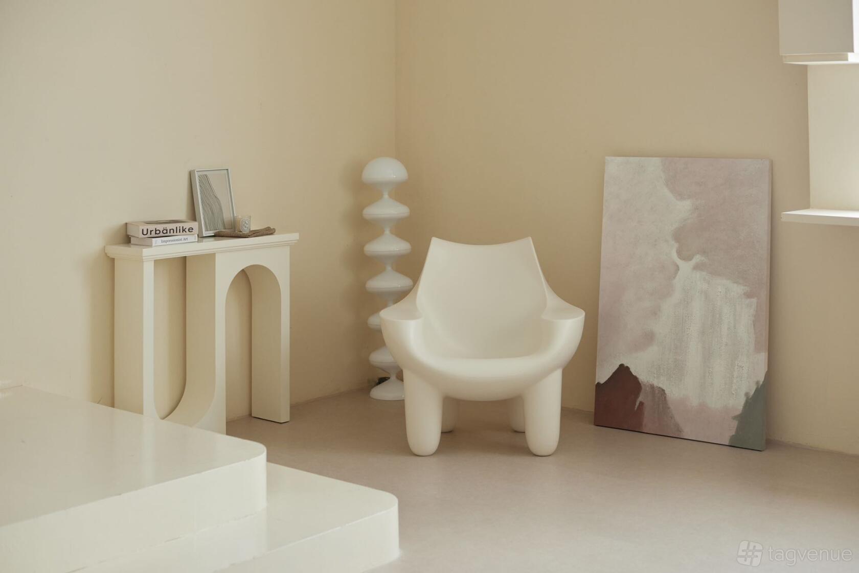 A photo studio with minimalist cream-colored walls, sculptural white armchair, abstract canvas, and modern decor at Vico Studio.