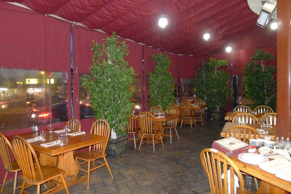 An outdoor dining area with wooden tables, matching chairs, potted green plants, and red canopy at Traktir Restaurant West Hollywood.