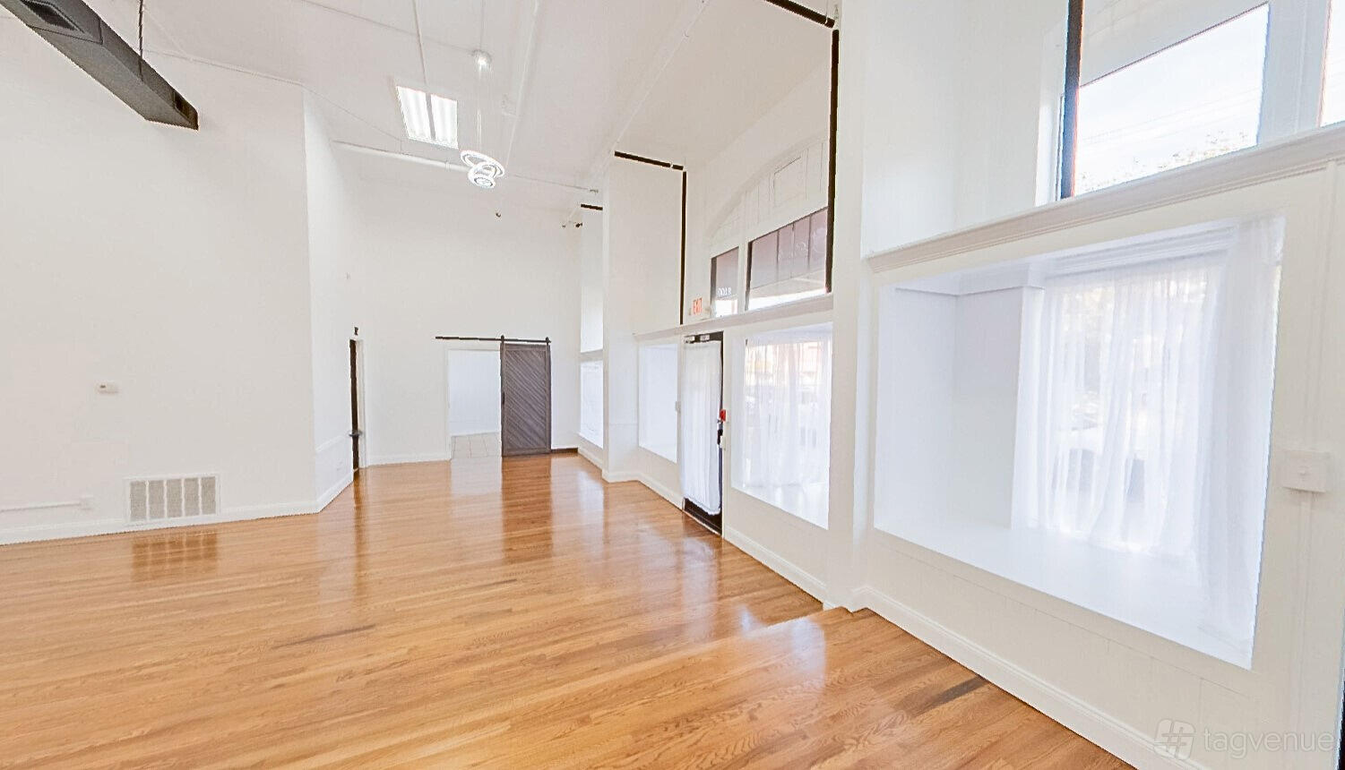 An event venue with hardwood floors, white walls, and large windows with sheer curtains at Sorella's Events, LLC.