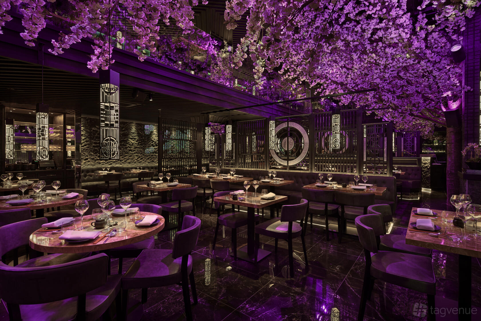 A restaurant with cherry blossom ceiling installations, moody purple lighting, and set round tables at TATTU Leeds.