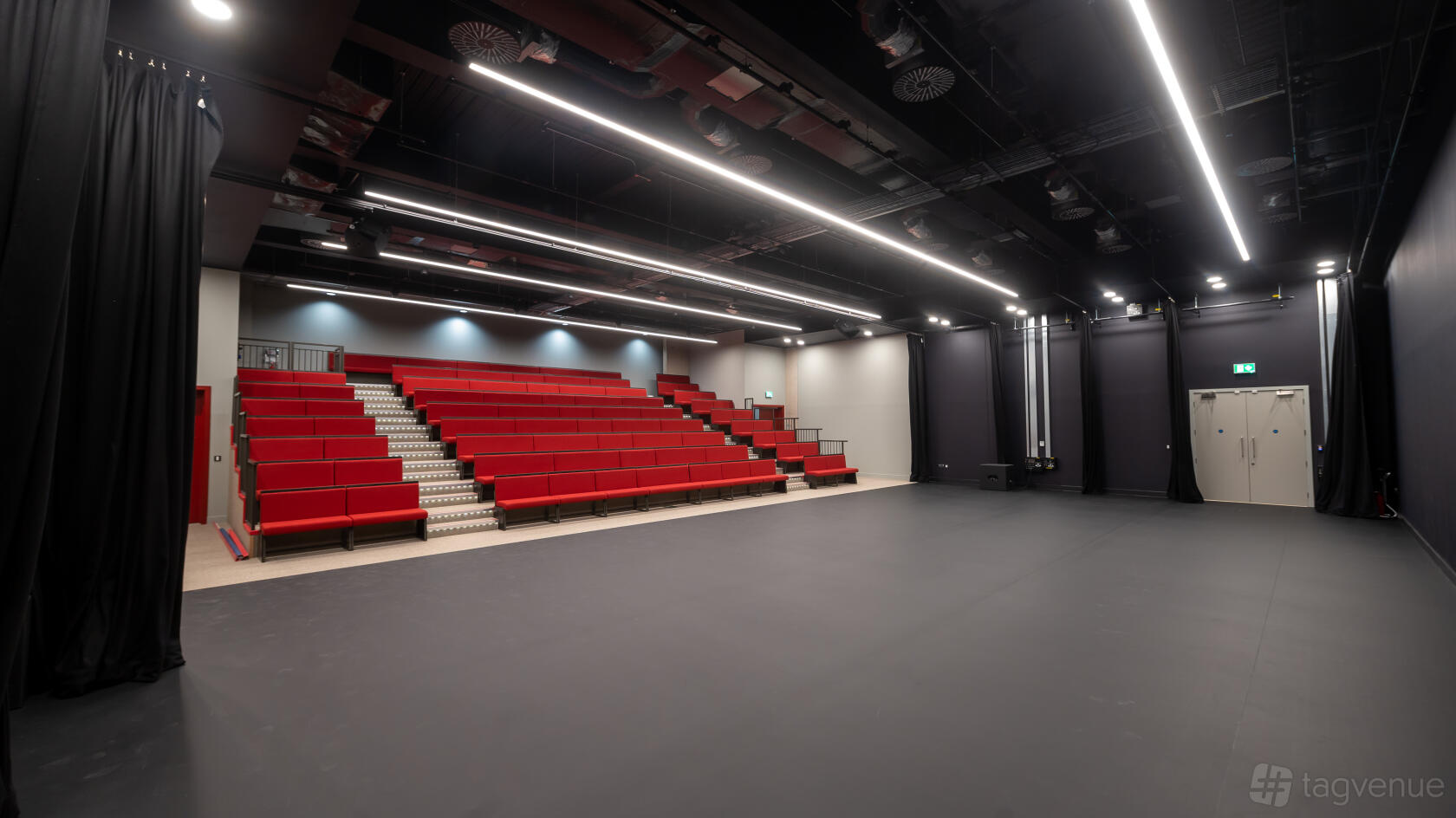 A dance studio with tiered red seating, black curtains, and overhead strip lighting at Royal Academy of Dance.