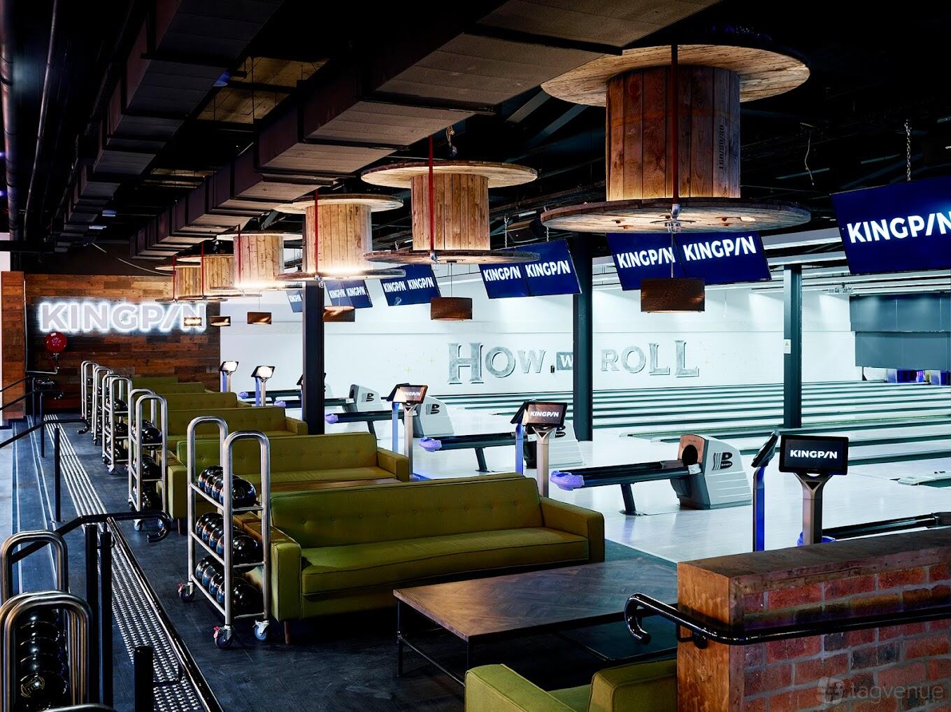 An event venue with multiple bowling lanes, neon signage, cushioned seating, and overhead screens at Kingpin North Strathfield.