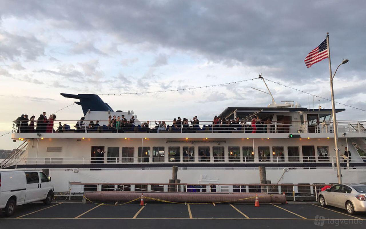 A two-level yacht with an upper outdoor deck, string lights, and groups of people at Yacht Events NYC.