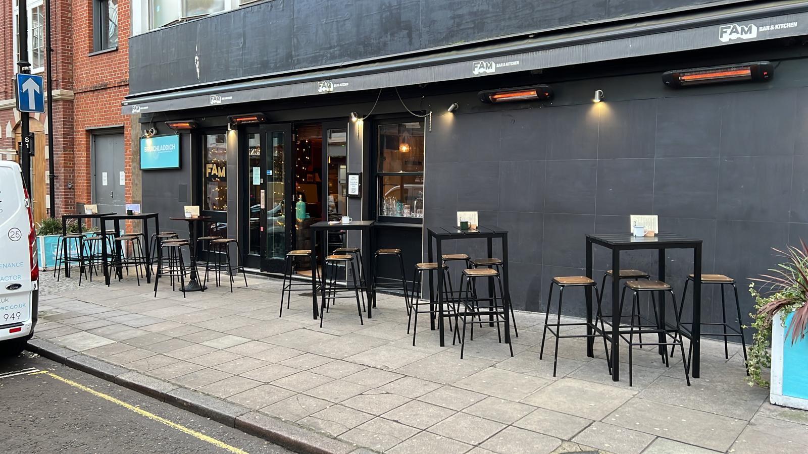 An urban bar with outdoor high tables and stools along the sidewalk at Fam Bar.