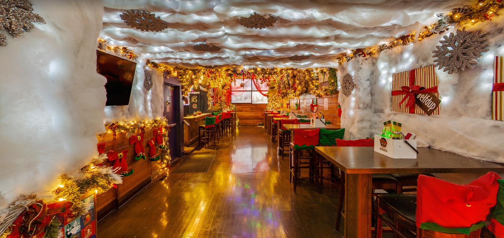 A bar decorated with holiday lights, faux snow on the ceiling, and stockings along wood-paneled walls at Elf’d Up.
