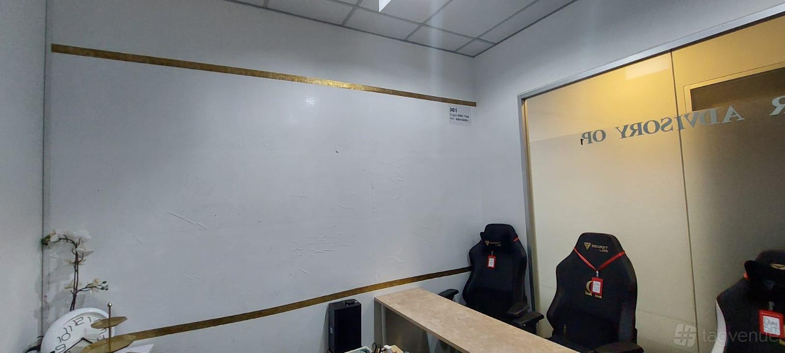 A training room with a large whiteboard wall, two black ergonomic chairs, and a wooden desk at Midview City Training Room.