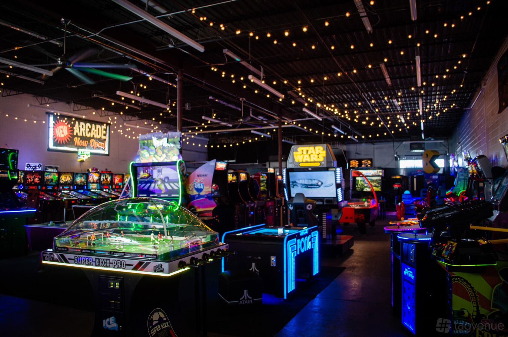 A warehouse venue with arcade games, neon lights, and string lighting at Super Awesome Fun Factory.