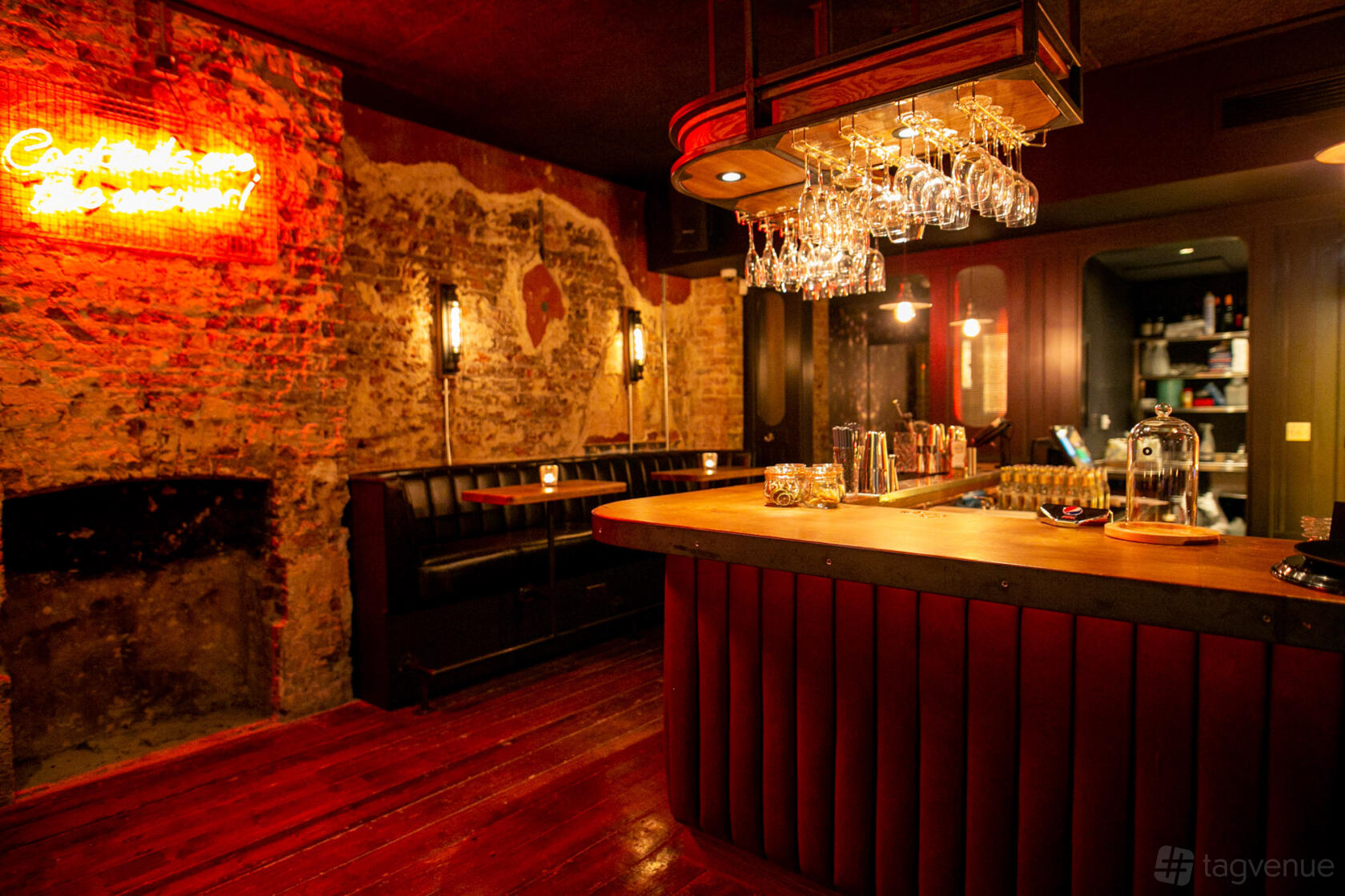 A cocktail bar with exposed brick walls, hanging glassware, a wooden counter, and booth seating at The Black Horse.
