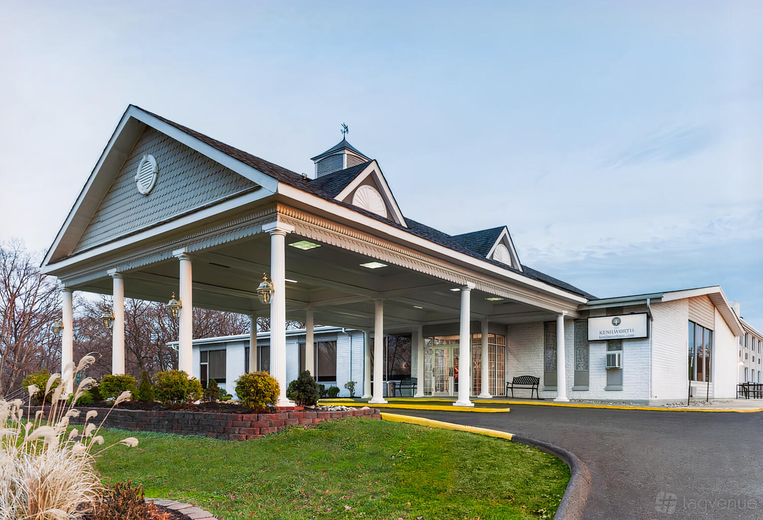 A hotel entrance with a covered driveway, white columns, and landscaped greenery at Kenilworth Inn.