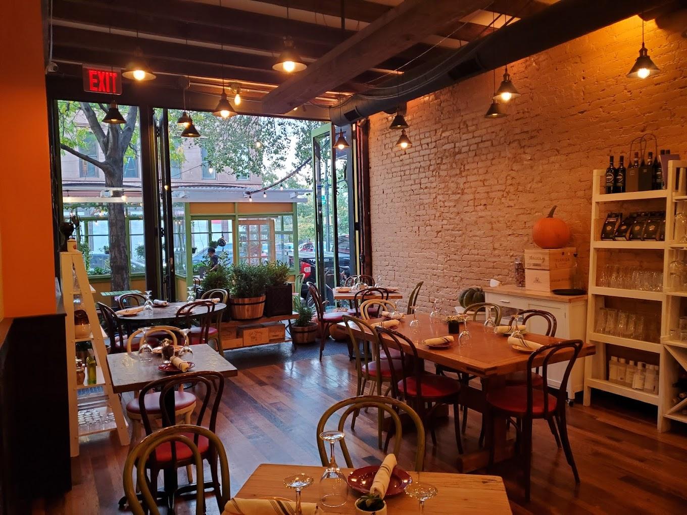 A restaurant with exposed brick walls, wooden floors, and large windows overlooking greenery at Osteria Brooklyn.