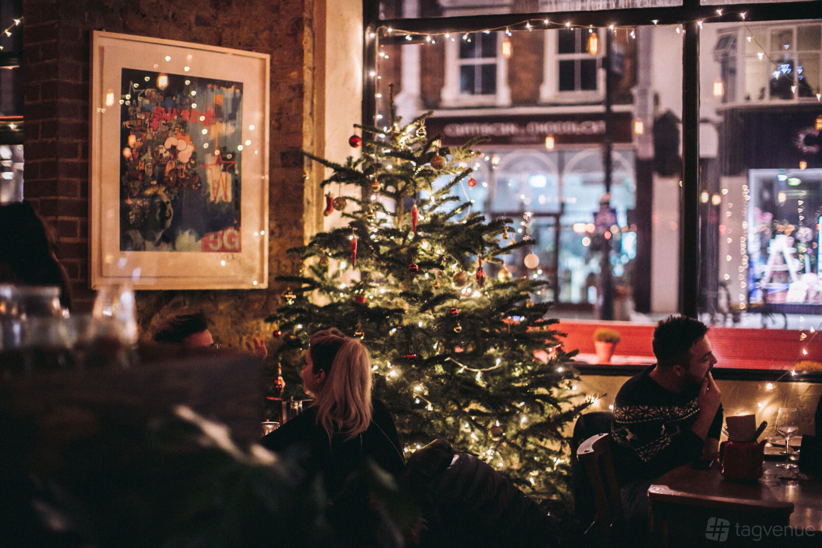 An event space in a bar with exposed brick walls, large windows, and a decorated Christmas tree at The Alice House Queen's Park.