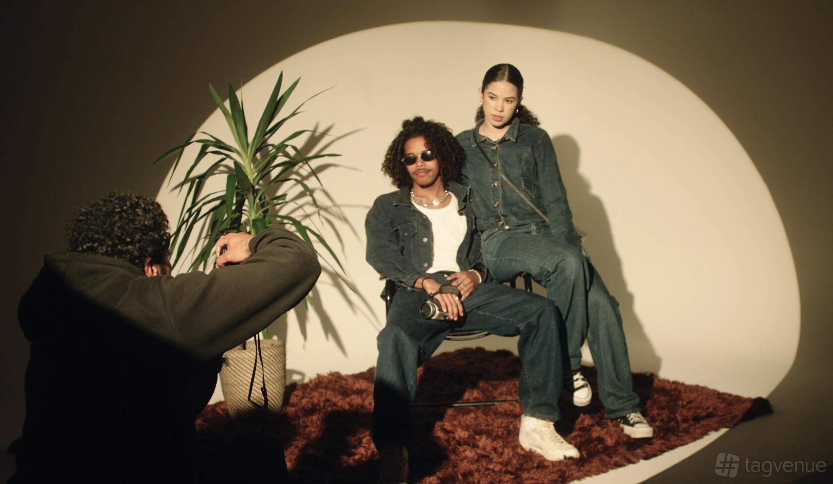 A photo studio with a brown rug, a spotlight on two people posing, and a potted plant at ON3 Studio.