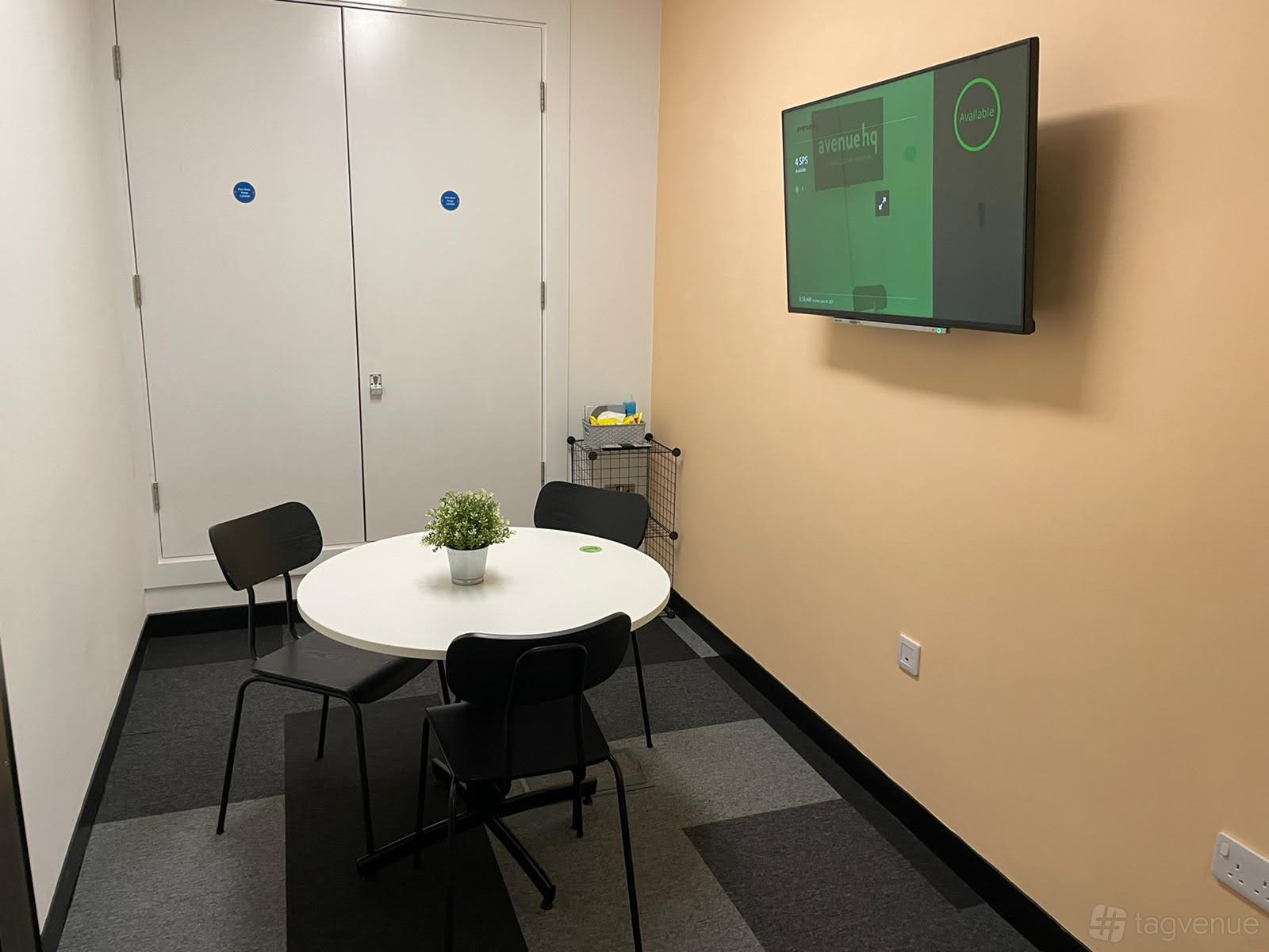 A coworking space with a small round table, four chairs, wall-mounted TV, and potted plant at Avenue HQ St Paul's Square.